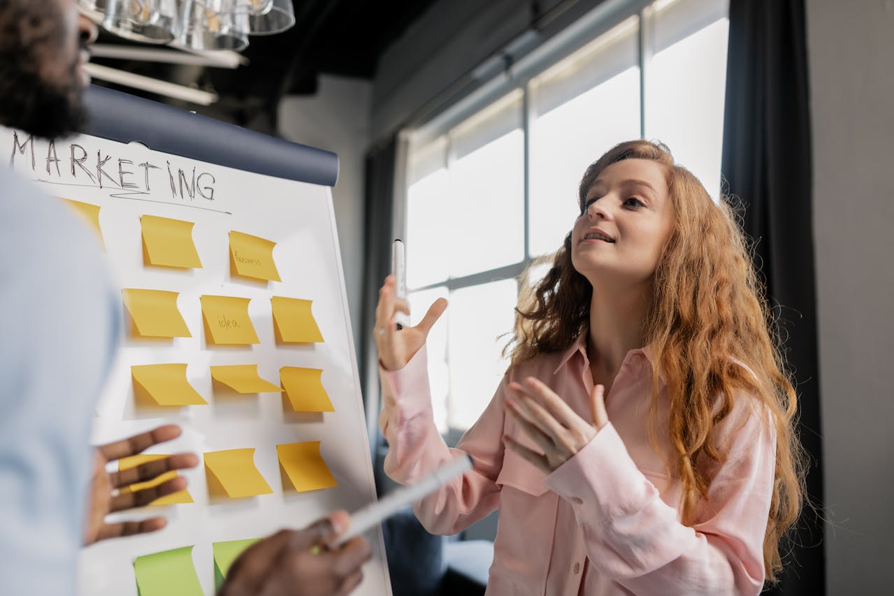 A Woman Talking About Marketing Near a Board with Post Its