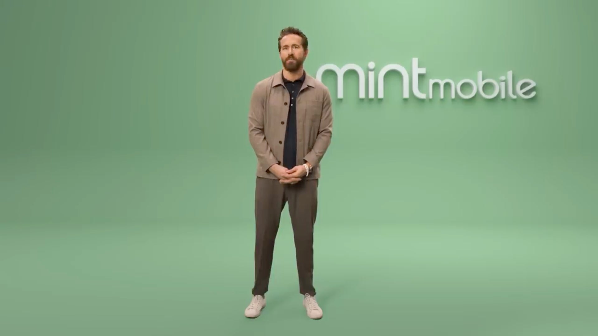 Ryan Reynolds standing against a wall with Mint Mobile written on it