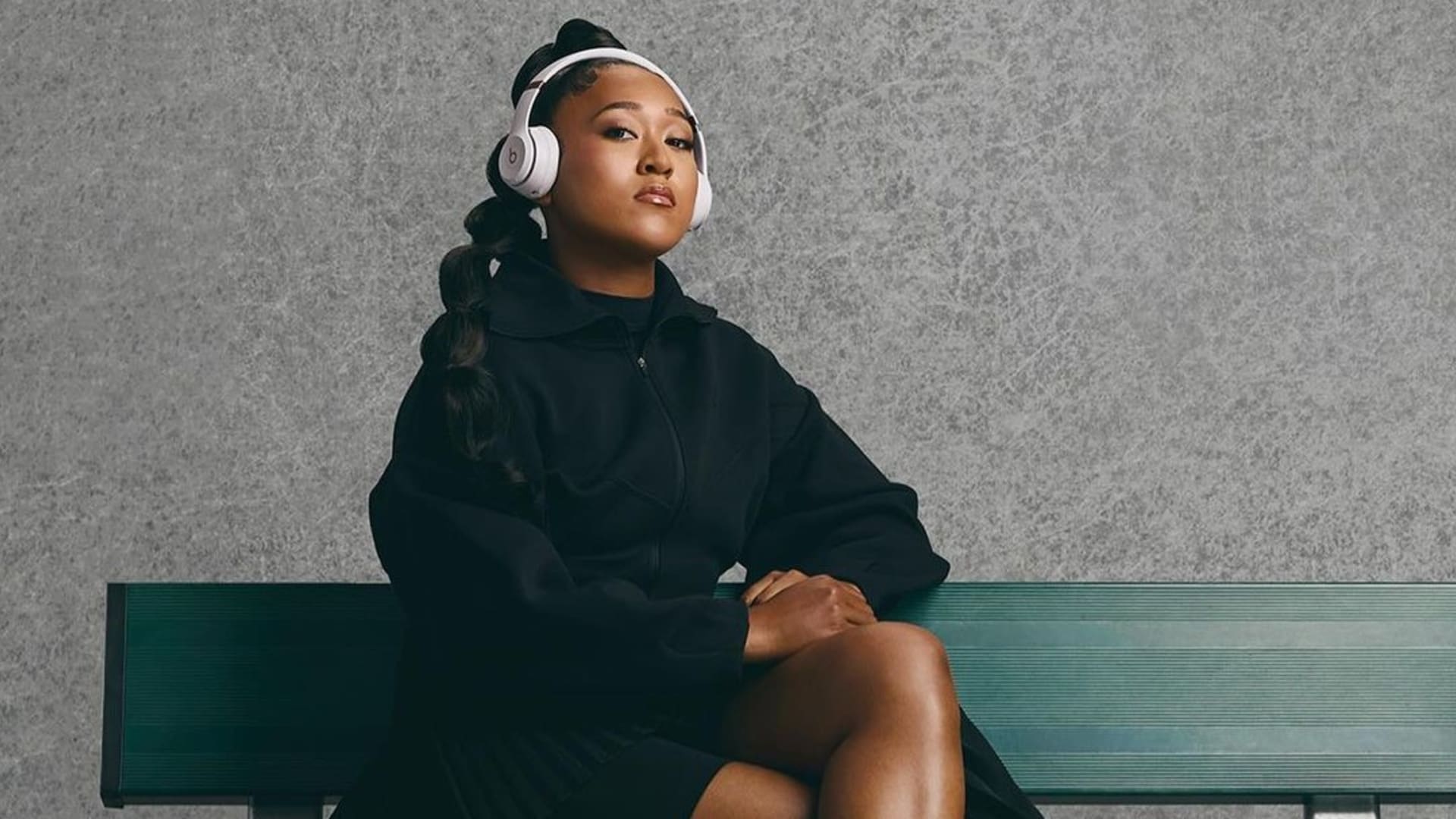 Naomi Osaka wearing headphones relaxed on a bench