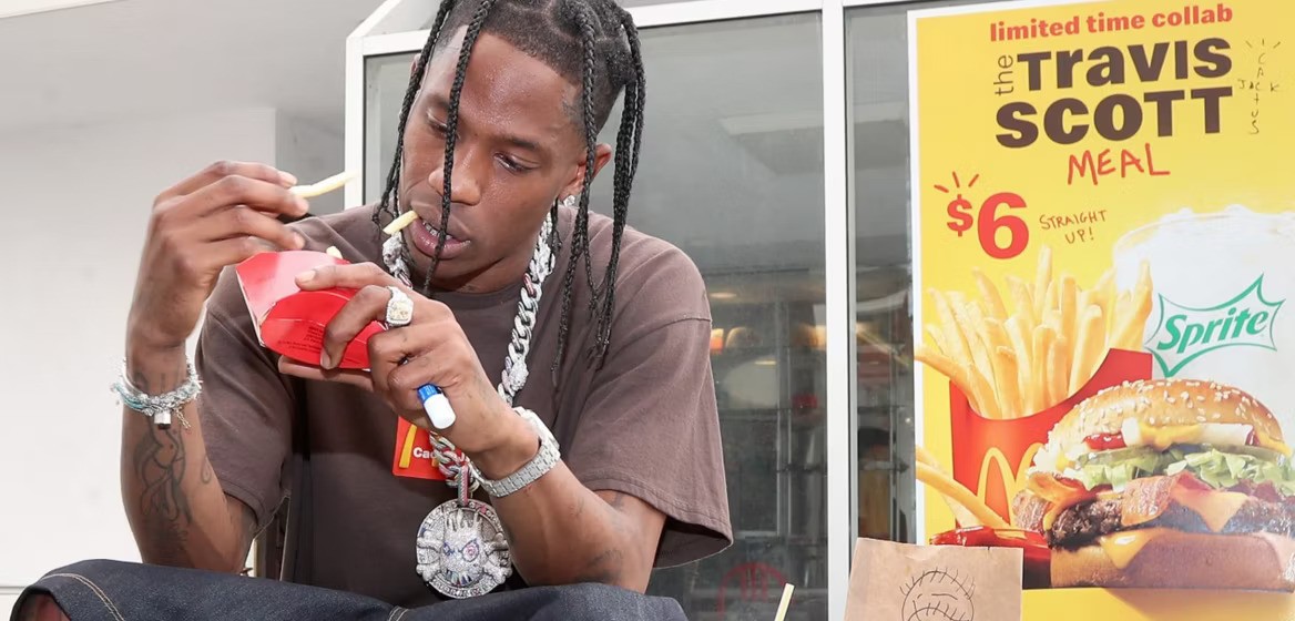 Travis Scott sitting on the ground, enjoying a burger